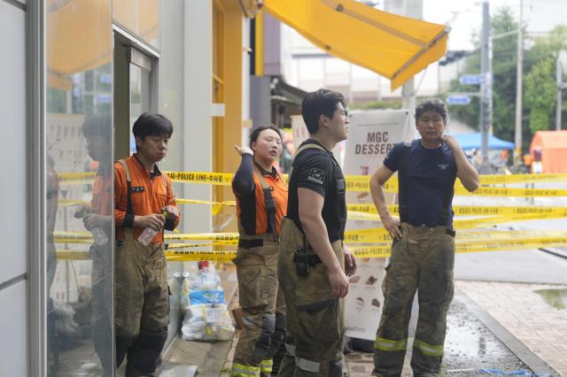 Exhausted firefighters in stained gear take a break behind police tape near a Coupang Warehouse 20260720 AJP Han Jun-gu