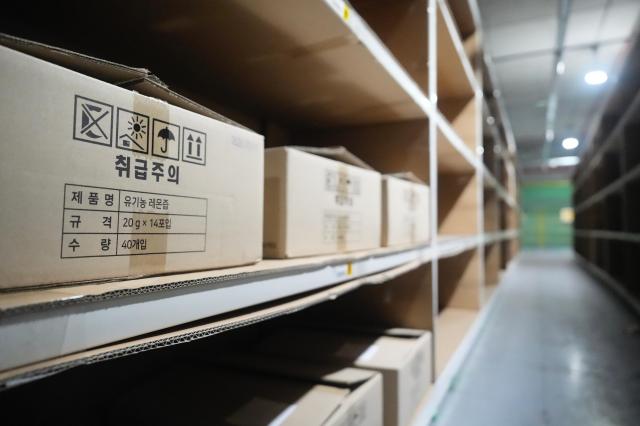 A photo of a labeled cardboard box marked Handle with Care containing organic lemon juice packets at the Coupang Warehouse shelf 20260720 AJP Han Jun-gu