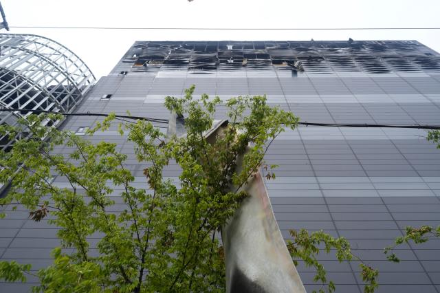 Burnt sheet-metal debris hangs from power lines near the Coupang warehouses loading dock with the collapsed upper floors of the building visible in the background AJP Han Jun-gu