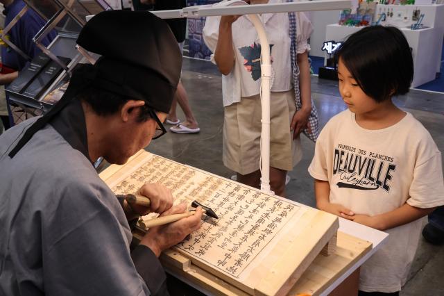 A child watches the traditional woodblock printing process at the Korea Pavilion the official host country exhibition held alongside the 48th session of the UNESCO World Heritage Committee at BEXCO in Busan on July 24 2026 AJP Yoo Na-hyun