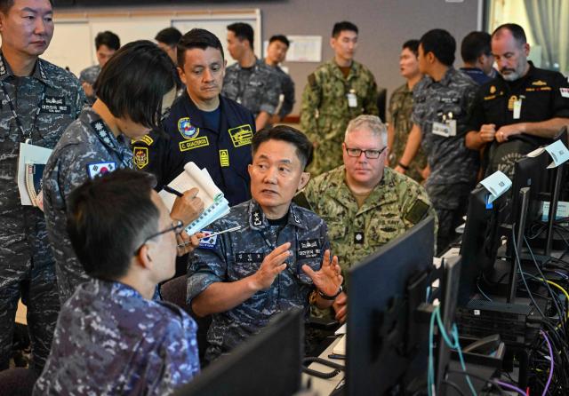 Rear Adm Kim In-ho center commander of the Republic of Korea Navy’s Naval Mobile Fleet and Combined Forces Maritime Component Commander for RIMPAC 2026 discusses maritime operations with combined staff at the Maritime Operations Center inside the Pacific Warfighting Center on July 7 2026 Courtesy of the ROK Navy
