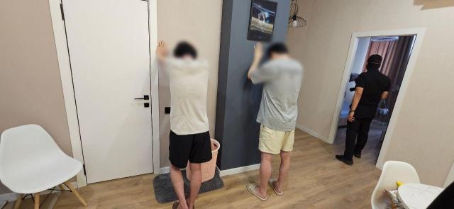Suspected members of the scam ring face the wall as officers search their hideout in Almaty, Kazakhstan. Courtesy of Korean National Police Agency