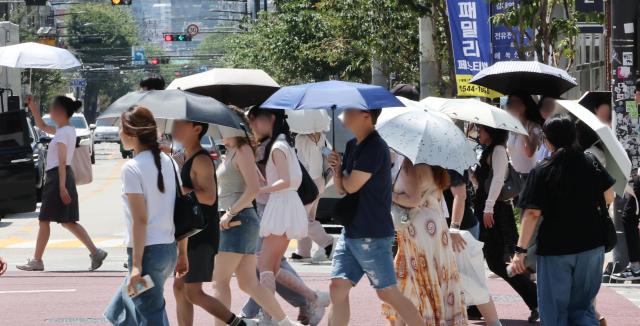 7日，市民和外籍游客撑着遮阳伞行走在首尔圣水洞街头。