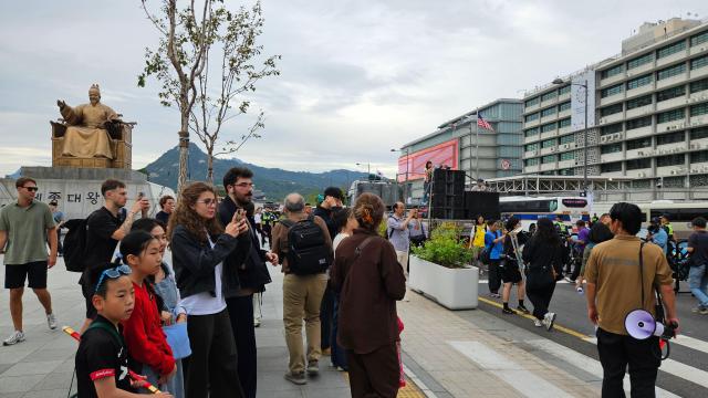 Foreign tourists at Gwanghwamun Square photograph protesters marching against South Korea’s possible troop deployment to the Strait of Hormuz in Jongno-gu central Seoul Sept 12 2026 The US Embassy is seen on the right AJP Lee Jung-woo 