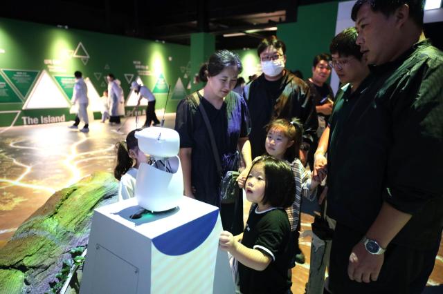 추석 연휴를 맞아 2026여수세계섬박람회를 찾은 가족 단위 관람객들이 주제섬에서 ‘AI 다섬이 도슨트’를 체험하고 있다 조직위는 연휴 직전 가족 관람객을 위한 체험 콘텐츠를 보강해 관람객들의 참여를 높였다사진재2026여수세계섬박람회조직위원회