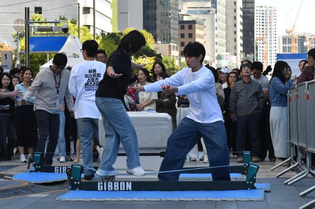 A visitor tries a practice slackline set up just above the pavement as staff members stand by to steady her at Cheonggye Plaza in central Seoul on Oct 1 2026 AJP Joonha Yoo